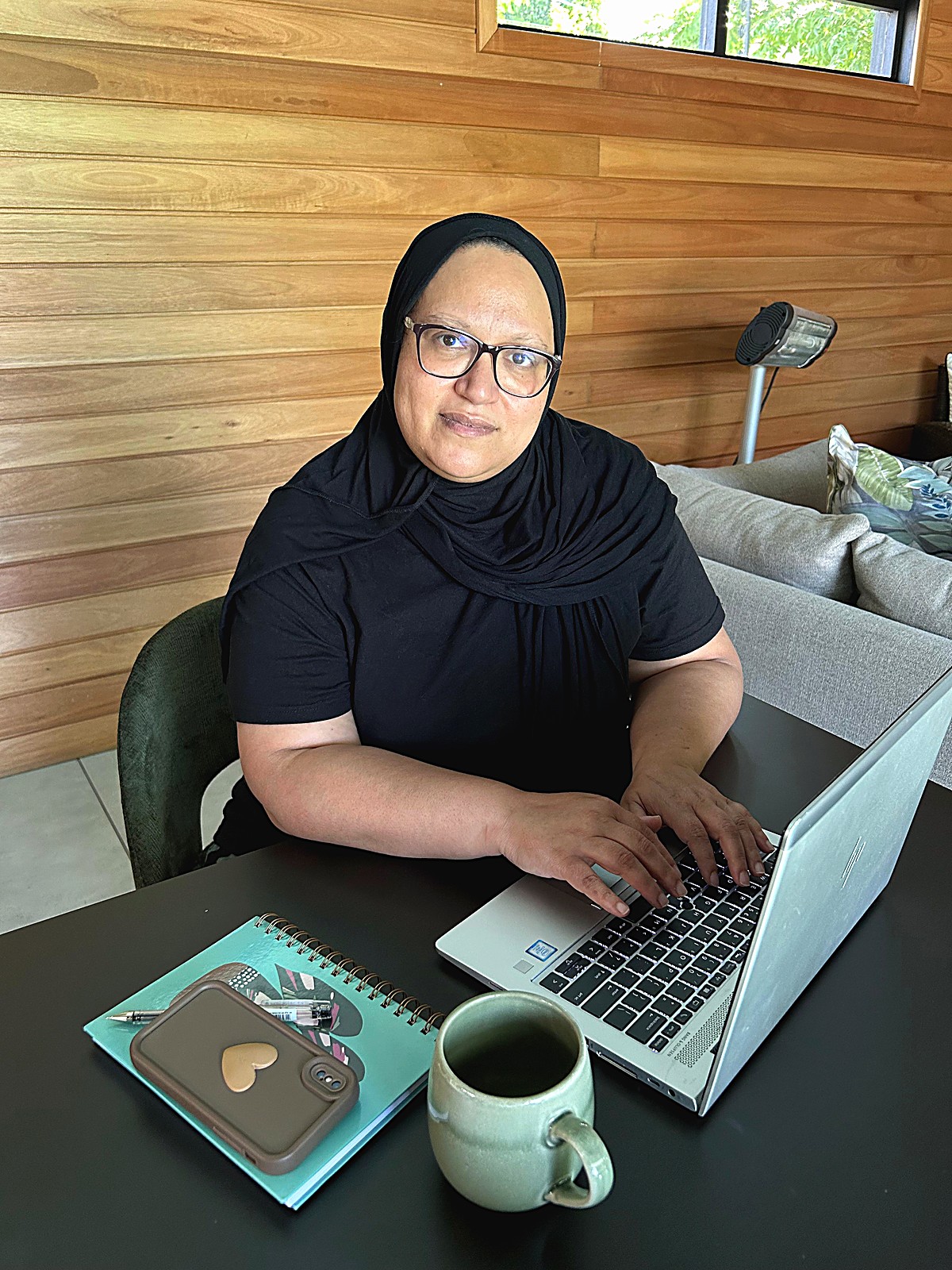 Fatima working at her laptop with a notebook and coffee