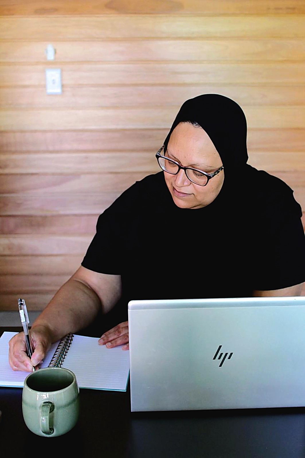 Fatima making notes in a notebook beside her laptop